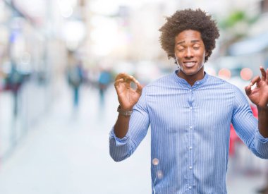 İzole arka plan üzerinde Afro Amerikalı adam rahatla ve gülümseyen gözlerle kapalı parmak jestle meditasyon yapıyor. Yoga kavramı.