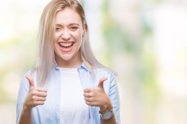 Genç Sarışın kadın el ile pozitif jest yapıyor izole arka plan başarı işareti yüzünden başparmak gülümseyen ve mutlu. Neşeli bir ifadeyle, kazanan jest kameraya bakıyor.