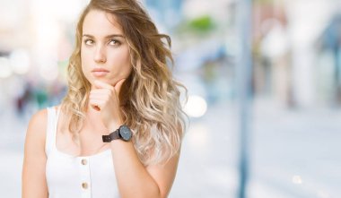 Genç güzel sarışın kadın elle çene düşünme hakkında soru, dalgın ifade izole arka plan yüzünden. Düşünceli yüzüyle gülümsüyor. Şüphe kavramı.