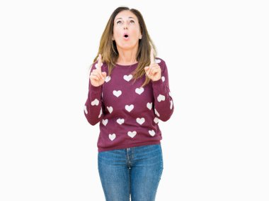 İzole arka plan üzerinde kalpler kazak giyen güzel orta yaş kadın hayrete ve yukarıya bakıyor ve parmakları ile işaret ve silah kaldırdı şaşırttı.