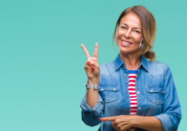 Orta yaş İspanyol kadın kıdemli mutlu yüz zafer işareti yaparken kameraya göz kırpıyor ile gülümseyen izole arka plan üzerinde. İki numaralı.