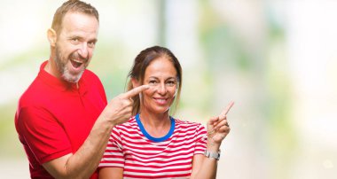 Orta yaş İspanyol çift kameraya bakarak yan el ve parmak ile işaret yüzünde kocaman bir gülümseme ile izole arka plan üzerinde aşık.