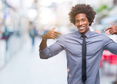 Yüzünde gülümseme ile kendinden emin görünüyorsun, kendini gururlu ve mutlu parmakları ile işaret izole arka plan üzerinde Afro Amerikalı iş adamı.