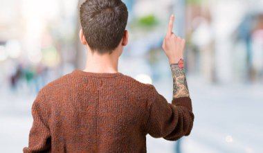 Genç yakışıklı adam giyen kış kazak izole üzerinde arka plan geriye doğru arkasında parmak eliyle işaret Posing