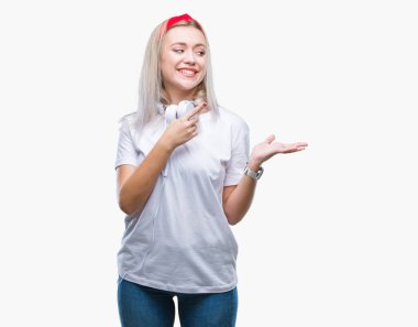 Üzerinden hayran ve el ile sunulması ve parmak ile işaret ederken kameraya gülümseyen izole arka plan müzik kulaklık giyen genç sarışın kadın.