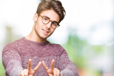 Zafer işareti yapıyor parmak gösterilen kamera seyir gülümseyen izole arka plan üzerinde gözlük takan yakışıklı delikanlı. İki numaralı.