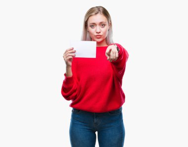 Sarışın genç kadın holding boş kağıt kartı kamera ve size parmak ile işaret izole arka plan üzerinde el işareti, pozitif ve kendinden emin bir jest ön