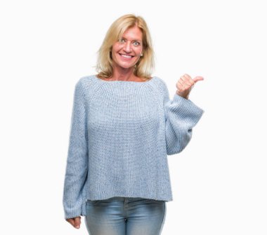 Seyir ve başparmak yanında yukarıyı mutlu yüz ile gülümseyen izole arka plan üzerinde kış kazak giyen orta yaş sarışın kadın.