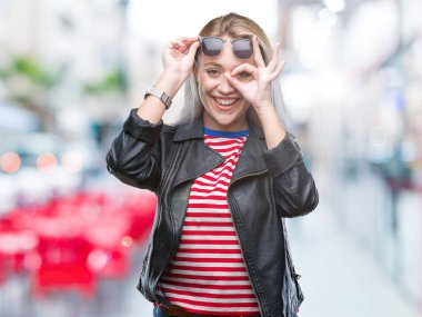 Mutlu yüz parmaklarıyla bakarak göz sarışın genç kadın giyiyor moda ceket ve el gülümseyen, ok jest yapıyor izole arka plan üzerinde güneş gözlüğü.