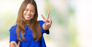 Zafer işareti yapıyor parmak gösterilen kamera seyir gülümseyen izole arka plan üzerinde mavi t-shirt giyen genç güzel esmer kadın. İki numaralı.