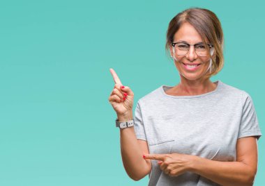 Kameraya bakarak yan el ve parmak ile işaret orta yaş üst düzey İspanyol kadın yüzünde kocaman bir gülümseme ile izole arka plan üzerinde gözlük.