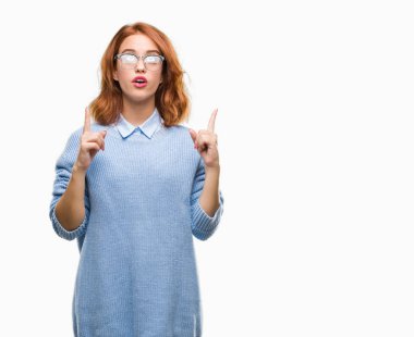 İzole arka plan kış kazak giyen genç güzel kadın hayrete ve yukarıya bakıyor ve parmakları ile işaret ve silah kaldırdı şaşırttı.