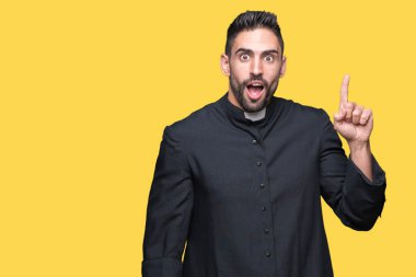 Genç Hıristiyan rahip izole arka plan üzerinde işaret parmağı kadar başarılı fikir. Çıktıktan ve mutlu. Bir numara.