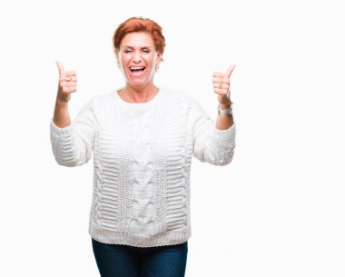 El ile pozitif jest yapıyor izole arka plan başarı işareti üzerinde kış kazak giyen Atrractive üst düzey beyaz Kızıl saçlı kadın başparmak gülümseyen ve mutlu. Neşeli bir ifadeyle, kazanan jest kameraya bakıyor.