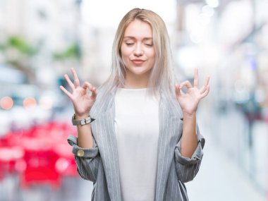 Genç Sarışın iş kadın giyiyor ceket izole arka plan üzerinde dinlenmek ve gülümseyen gözlerle kapalı parmak jestle meditasyon yapıyor. Yoga kavramı.