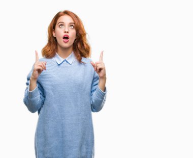 İzole arka plan kış kazak giyen genç güzel kadın hayrete ve yukarıya bakıyor ve parmakları ile işaret ve silah kaldırdı şaşırttı.