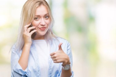 Genç Sarışın kadın konuşmaya smarpthone izole arka plan üzerinde mutlu ok işareti yapıyor büyük gülümseme ile kullanarak başparmak yukarı parmaklarıyla, mükemmel işareti