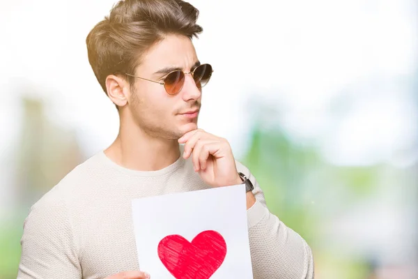 Joven Hombre Guapo Sosteniendo Tarjeta Con Corazón Rojo Sobre Fondo — Foto de Stock