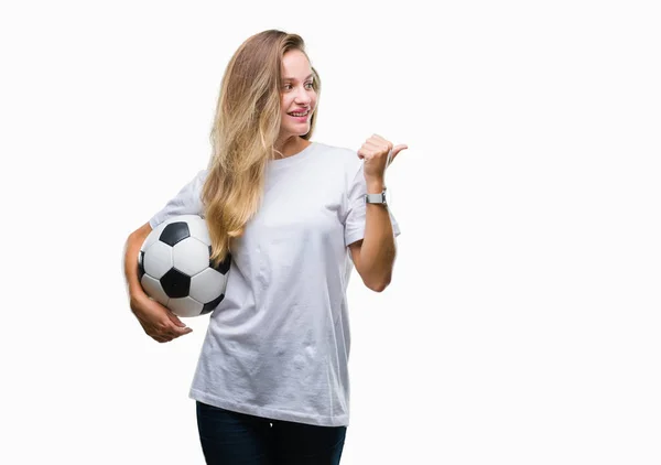 年轻美丽的金发碧眼的女人拿着足球在孤立的背景指向和显示与快乐的脸微笑的一侧 — 图库照片