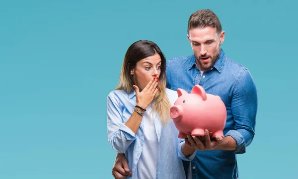 Young couple in love holding piggy bank over isolated background cover mouth with hand shocked with shame for mistake, expression of fear, scared in silence, secret concept