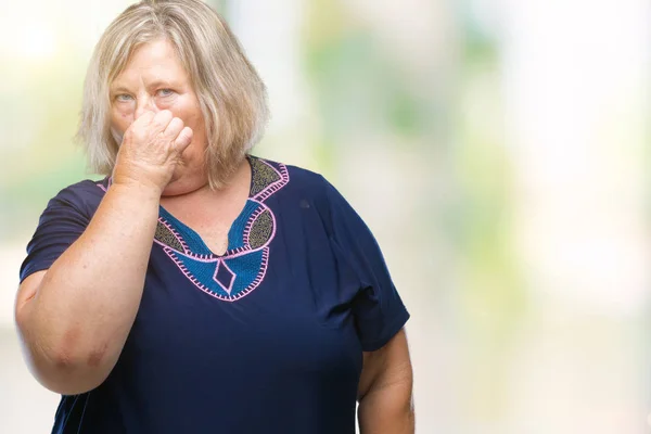 Senior plus size caucasian woman over isolated background smelling something stinky and disgusting, intolerable smell, holding breath with fingers on nose. Bad smells concept.