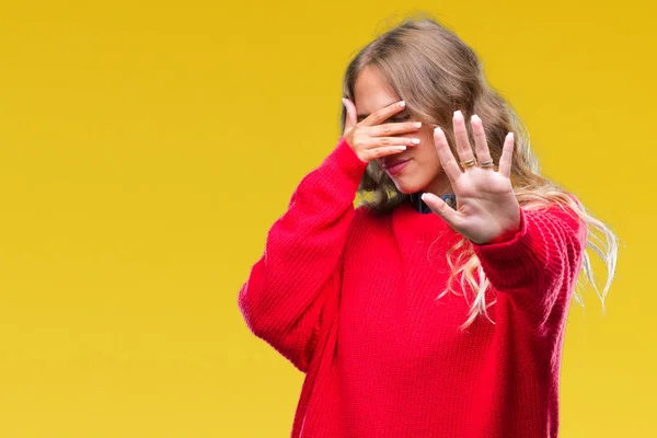 Beautiful young blonde woman wearing winter sweater over isolated background covering eyes with hands and doing stop gesture with sad and fear expression. Embarrassed and negative concept.