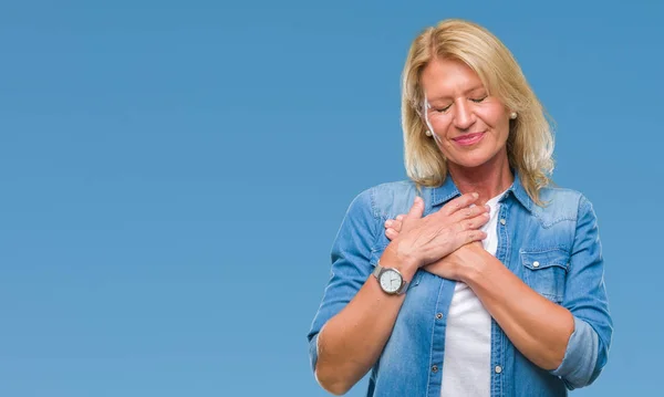 Middle age blonde woman over isolated background smiling with hands on chest with closed eyes and grateful gesture on face. Health concept.