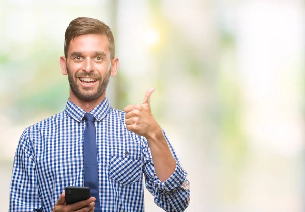 年轻的 Hadsome 人短信发送信息使用智能手机在孤立的背景下快乐的大微笑做 拇指与手指 优秀的标志 — 图库照片