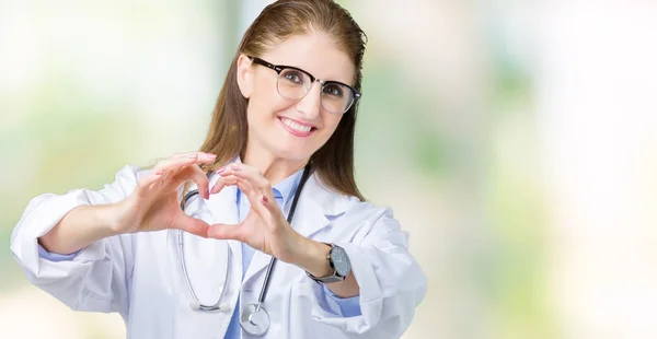 中年成熟的医生妇女穿着医疗外套在孤立的背景微笑在爱中显示心脏符号和形状用手 浪漫的概念 — 图库照片