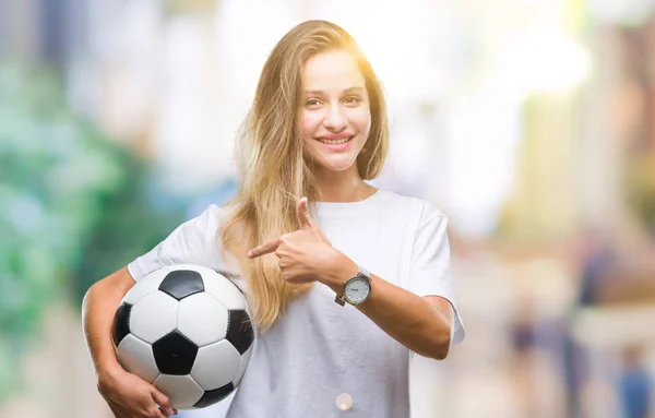 非常に幸せな手と指で指しての孤立した背景にサッカー ボールを保持している若い美しいブロンドの女性 — ストック写真
