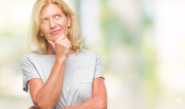 Middle age blonde woman over isolated background looking confident at the camera with smile with crossed arms and hand raised on chin. Thinking positive.