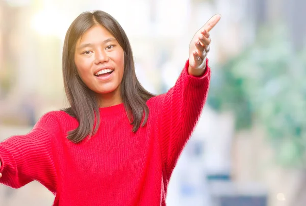 若いアジア女性はハグするため両手を広げて笑みを浮かべてカメラを見て孤立の背景に冬のセーターを着ています 晴れやかな表情の受け入れ幸せ — ストック写真
