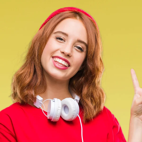 Genç güzel hipster kadın kulaklık ve mutlu yüz zafer işareti yaparken kameraya göz kırpıyor ile gülümseyen kap giyen izole arka plan yüzünden. İki numaralı.