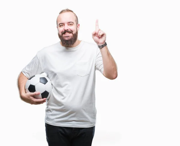 年轻的高加索嬉皮士男子拿着足球在孤立的背景惊讶与想法或问题指向手指与愉快的面孔 — 图库照片