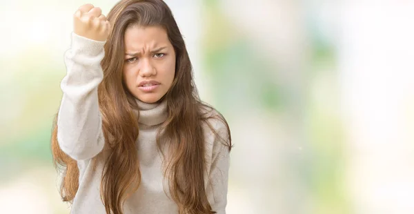Young beautiful brunette woman wearing turtleneck sweater over isolated background angry and mad raising fist frustrated and furious while shouting with anger. Rage and aggressive concept.