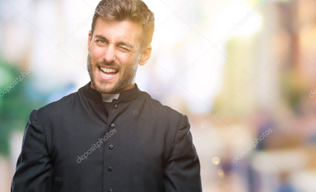 Young catholic christian priest man over isolated background winking looking at the camera with sexy expression, cheerful and happy face.