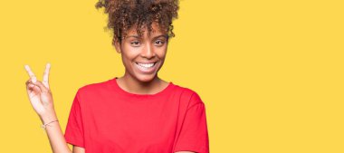 Güzel genç Afro-Amerikan kadın mutlu yüz zafer işareti yaparken kameraya göz kırpıyor ile gülümseyen izole arka plan yüzünden. İki numaralı.