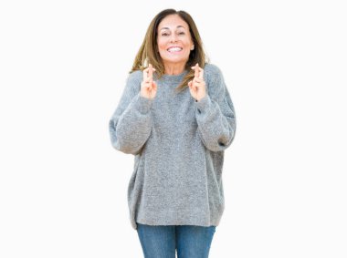 Umut ve gözleri kapalı geçiş parmaklarıyla gülümseyen izole arka plan üzerinde kış kazak giyen güzel orta yaş kadın. Şans ve batıl kavramı.