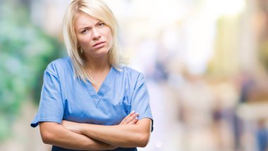 Genç güzel sarışın hemşire doktor kadın izole arka plan şüpheci ve çapraz kolları olan yüzündeki gergin, onaylamayan ifade yüzünden. Negatif kişi.