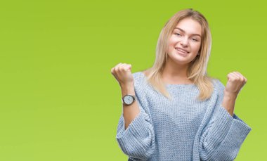 İzole arka plan üzerinde kutluyor kış kazak giyen genç beyaz kadın şaşırttı ve başarı için kaldırdı kollarını açarak hayret ve gözleri açık. Kazanan kavramı.