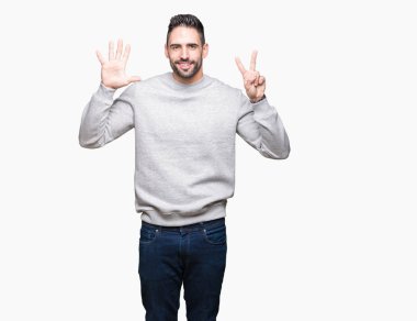 Gösterilen arka plan üzerinde sweatshirt giyen genç yakışıklı adam izole ve parmakları ile işaret kendinden emin ve mutlu gülümseyerek süre yedi numara.