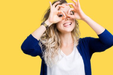 Güzel sarışın genç kadın dilini, parmaklarının arasından baktığını yapışmasını dürbün gibi ok jest yapıyor izole arka plan üzerinde. Deli ifade.