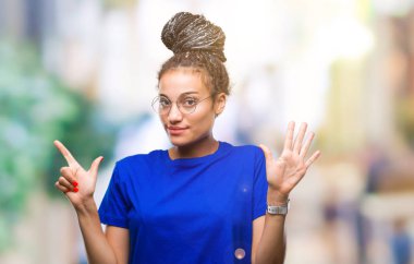 Saç Afro-Amerikan Kız izole arka plan üzerinde gösterilen gözlüklü genç örgülü ve parmakları ile işaret kendinden emin ve mutlu gülümseyerek süre yedi numara.