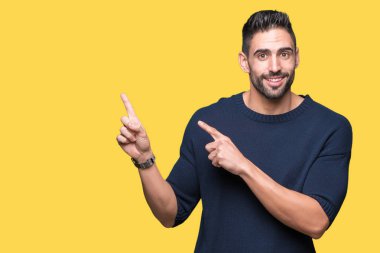 Gülümseyen ve iki elleri ve parmakları ile tarafına işaret kamera bakarak izole arka plan üzerinde kazak giyen genç yakışıklı adam.