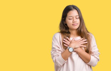 İle gülümseyen izole arka plan üzerinde pembe kazak giyen genç güzel esmer kadın kapalı gözler ve yüzünde minnettar jest ile göğüs üzerinde eller. Sağlık kavramı.