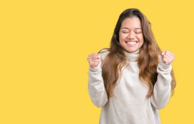 Zafer kutluyor gülümseyen izole arka kolları olan başarı için heyecan üzerinde boğazlı kazak giyen genç güzel esmer kadın kaldırdı. Kazanan kavramı.