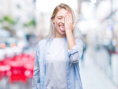 Sarışın genç kadın el yüz ve sürpriz duygu kendinden emin gülümseme ile tek gözüyle kapsayan izole arka plan üzerinde.