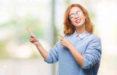 İzole arka plan gülümseyen ve iki elleri ve parmakları ile tarafına işaret kamera bakarak kış kazak giyen genç güzel kadın.