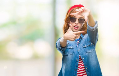 Genç güzel kadın elle yapma çerçeve ve parmakları ile mutlu yüz gülümseyen güneş gözlüğü takıyor izole arka plan yüzünden. Yaratıcılık ve Fotoğrafçılık kavramı.