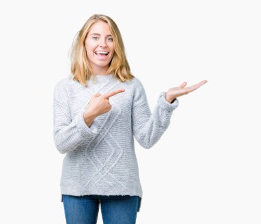 Hayret ve el ile sunulması ve parmak ile işaret ederken kameraya gülümseyen izole arka plan üzerinde kış kazak giyen güzel genç kadın.